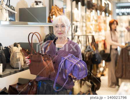 Elderly woman chooses handbag in accessories boutique 140021796