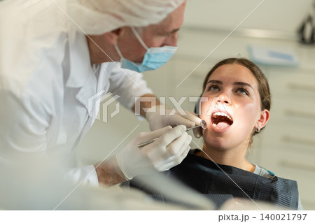Mature man doctor dentist in white coat examines oral cavity of girl patient in dentistry. Mature man doctor dentist in white coat examines oral cavity of girl patient in dentistry. 140021797
