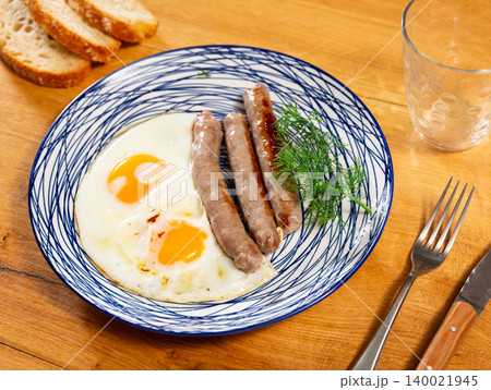 Fried eggs served with sausages on plate 140021945