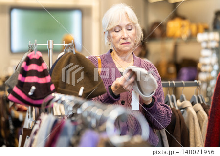 Eldery woman chooses hat in accessories store 140021956