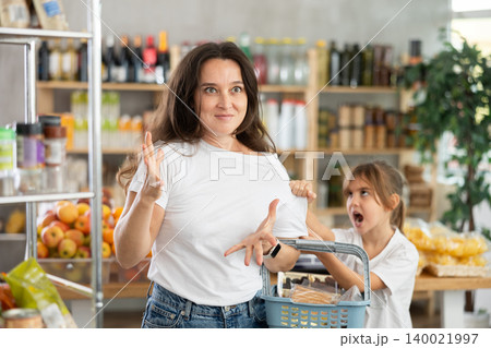 Capricious daughter screams and demands to buy sweets at the store. Mom is shocked by the naughty child Capricious daughter screams and demands to buy sweets at the store. Mom is shocked by the naughty child 140021997