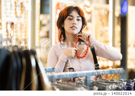 Attentive young girl choosing necklace in clothing store 140022014