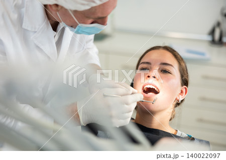 Mature man doctor dentist in white coat examines oral cavity of girl patient in dentistry. 140022097