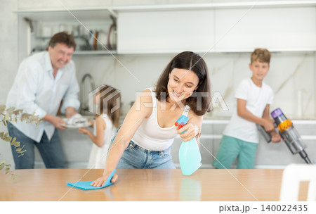 Positive mother cleaning the surface of kitchen table Positive mother cleaning the surface of kitchen table 140022435