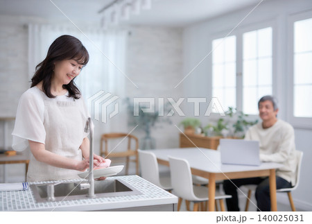 キッチンでお皿を拭きながら笑顔で話す60代女性と男性 140025031