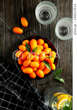 Kumquats in a black tray with green leaves and glasses 140025614