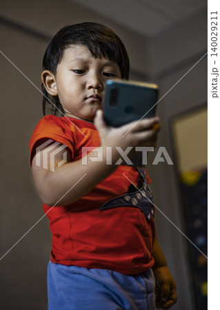 Toddler Using Smartphone To Call His Mother In The Room. Cute asian little boy pretending to make a phone call to his mom, ideal for family lifestyle, technology and childhood development themes. Toddler Using Smartphone To Call His Mother In The Room. Cute asian little boy pretending to make a phone call to his mom, ideal for family lifestyle, technology and childhood development themes. 140029211