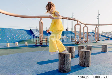 Little girl balancing on playground stumps, focused and playing on a sunny day. Little girl balancing on playground stumps, focused and playing on a sunny day. 140030712