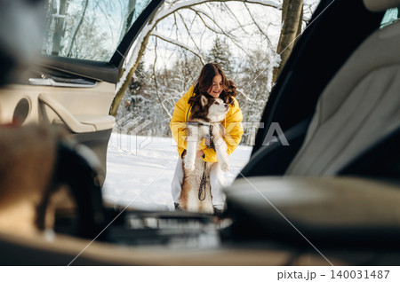 Woman in yellow jacket is lifting a dog from a car parked in a snowy landscape with trees in the background during a winter outing with copy space Woman in yellow jacket is lifting a dog from a car parked in a snowy landscape with trees in the background during a winter outing with copy space 140031487