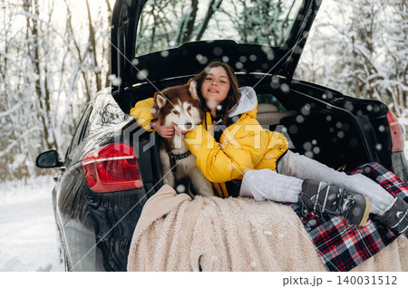 Young girl in yellow jacket cuddling a Siberian Husky dog in the trunk of a car surrounded by snow-covered trees during winter outdoor adventure with cozy blankets Young girl in yellow jacket cuddling a Siberian Husky dog in the trunk of a car surrounded by snow-covered trees during winter outdoor adventure with cozy blankets 140031512