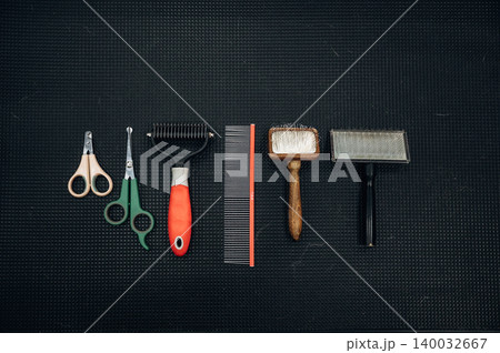Grooming tools for dogs arranged on a black textured surface, including scissors, combs, and brushes for effective pet care and grooming routines 140032667
