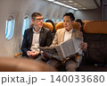 Businessman in brown suit on trip holding business newspaper while reading in plane during flight 140033680
