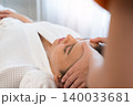 Asian woman in white towel with eyes closed lying in relaxation and enjoying facial massage at spa salon 140033681