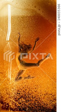 Graceful female dancer leaping inside golden beer bubbles close up. Graceful female dancer leaping inside golden beer bubbles close up. 140035366