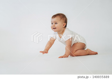 Baby crawling on a white background wearing a short-sleeve onesie, smiling and reaching forward with one hand, showcasing early mobility and development Baby crawling on a white background wearing a short-sleeve onesie, smiling and reaching forward with one hand, showcasing early mobility and development 140035889