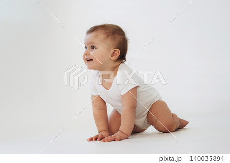 Baby crawling on hands and knees wearing a white onesie against a plain white background, showcasing a playful expression and natural curiosity Baby crawling on hands and knees wearing a white onesie against a plain white background, showcasing a playful expression and natural curiosity 140035894