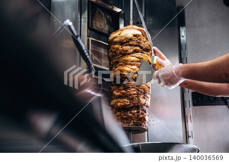 Chef slicing vertical stack of grilled meat with large knife in commercial kitchen, metal equipment and countertop visible in the background Chef slicing vertical stack of grilled meat with large knife in commercial kitchen, metal equipment and countertop visible in the background 140036569