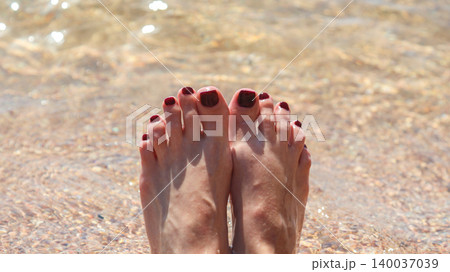 Women's feet with painted nails on the sand in clear sea water Women's feet with painted nails on the sand in clear sea water 140037039