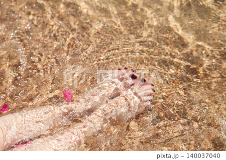 Women's feet with painted nails on the sand in clear sea water Women's feet with painted nails on the sand in clear sea water 140037040