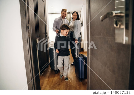 Family of three entering a hotel room with luggage, showcasing a modern interior design and wooden flooring, creating a welcoming atmosphere for travelers Family of three entering a hotel room with luggage, showcasing a modern interior design and wooden flooring, creating a welcoming atmosphere for travelers 140037132