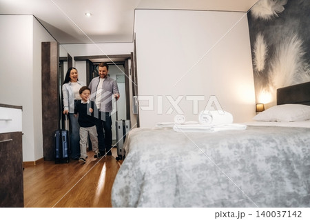 Family entering hotel room with luggage, modern decor featuring a bed, towels, and wooden flooring, welcoming atmosphere for travelers and guests Family entering hotel room with luggage, modern decor featuring a bed, towels, and wooden flooring, welcoming atmosphere for travelers and guests 140037142