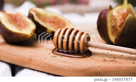 Wooden Honey Dipper with Fresh Halved Figs and Honey on a Rustic Cutting Board Wooden Honey Dipper with Fresh Halved Figs and Honey on a Rustic Cutting Board 140037977