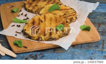 Grilled Pineapple Slices with Cloves and Fresh Mint on a Wooden Board 140037980