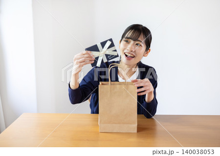 明るい室内で紙袋からプレゼント箱を取り出して微笑む日本人の若い女性 140038053