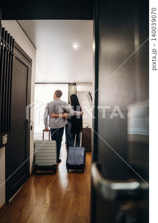Couple standing in hotel room with luggage, embracing each other while looking at the interior design and furnishings of the modern accommodation Couple standing in hotel room with luggage, embracing each other while looking at the interior design and furnishings of the modern accommodation 140039070