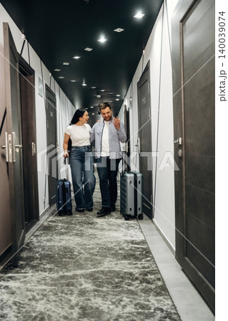Couple walking in hotel corridor with luggage, modern doors and stylish lighting visible, showcasing contemporary interior design and travel experience 140039074