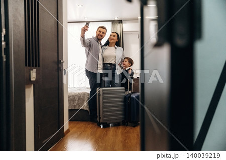 Family of three taking a selfie inside a modern hotel room, with luggage placed on the floor and a bed visible in the background Family of three taking a selfie inside a modern hotel room, with luggage placed on the floor and a bed visible in the background 140039219
