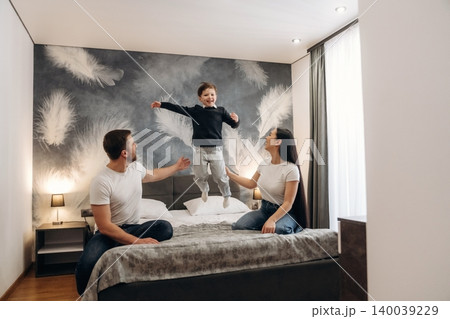 Family enjoying time together in a modern hotel room with a child jumping on the bed, featuring stylish decor and soft lighting in a cozy atmosphere Family enjoying time together in a modern hotel room with a child jumping on the bed, featuring stylish decor and soft lighting in a cozy atmosphere 140039229
