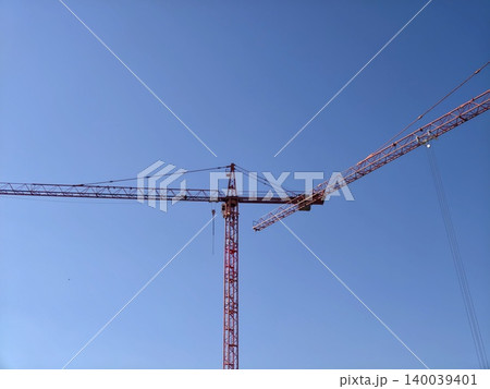 Elegant crane structure against sky. Stylized tower crane with intersecting red beams in open atmosphere Elegant crane structure against sky. Stylized tower crane with intersecting red beams in open atmosphere 140039401