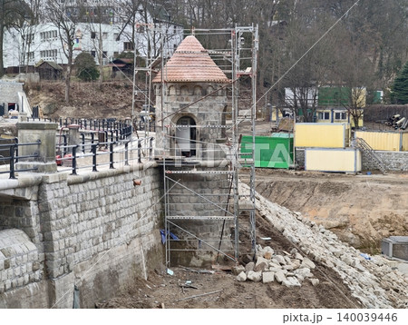 Scaffolding covers historic riverside tower. Stone foundation exposed during renovation of turret 140039446