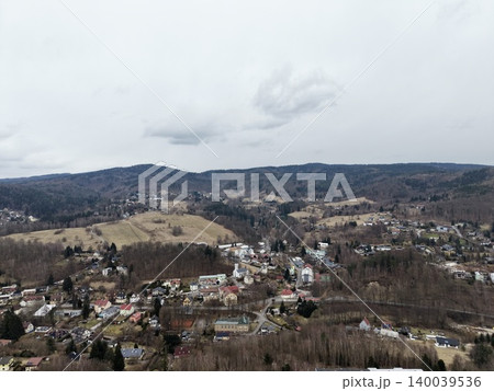 Scattered houses among leafless trees from above. Panoramic shot of village nestled in mountain landscape Scattered houses among leafless trees from above. Panoramic shot of village nestled in mountain landscape 140039536