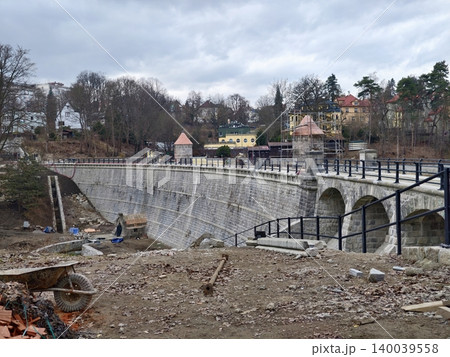 Old masonry bridge under overcast sky. Historical stone structure with river and village scenery Old masonry bridge under overcast sky. Historical stone structure with river and village scenery 140039558