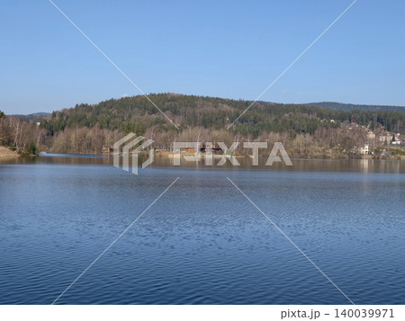Serene lake with forested hills. Peaceful waters reflecting distant woodland and cabin scenes Serene lake with forested hills. Peaceful waters reflecting distant woodland and cabin scenes 140039971