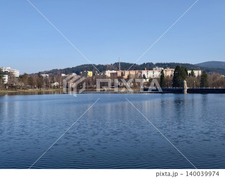 Peaceful lakeside scene. Calm water reflects urban treescape. Quiet neighborhood by tranquil water with hills 140039974