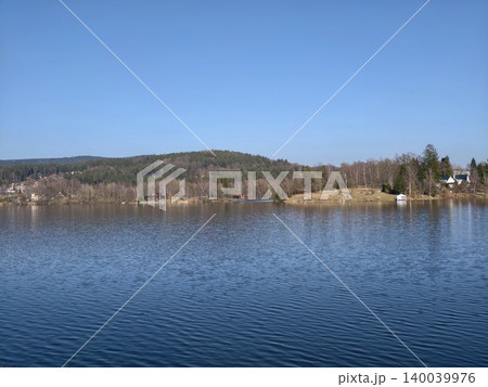Idyllic outdoor setting showcasing serene lake bordered by hills and trees under bright sky Idyllic outdoor setting showcasing serene lake bordered by hills and trees under bright sky 140039976