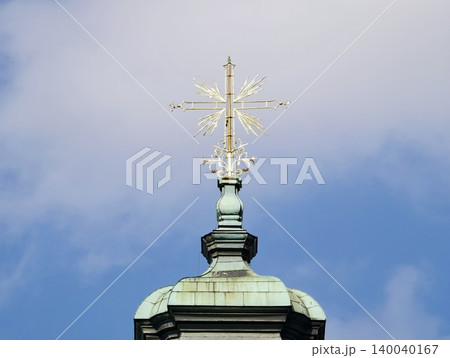 Intricately designed gilded cross with copper dome reflects sunlight against cloudy sky background 140040167