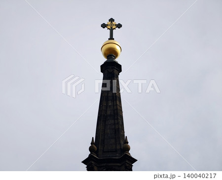 Elaborate pinnacle with gilded orb. Intricate steeple crowned with golden spherical cross against clouds Elaborate pinnacle with gilded orb. Intricate steeple crowned with golden spherical cross against clouds 140040217