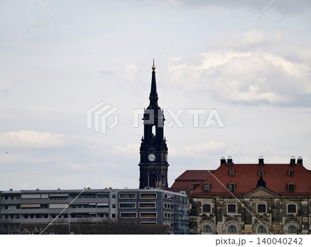 Skyscraper amid clouds. Majestic Gothic steeple rises over crowded urban environment with overcast skies Skyscraper amid clouds. Majestic Gothic steeple rises over crowded urban environment with overcast skies 140040242