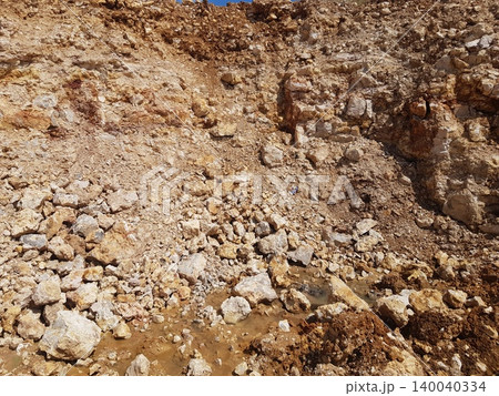 Coarse, light-colored limestone rocks and loose soil blanket this raw excavation site, showcasing a rugged, earthy texture with muddy puddles at the base 140040334
