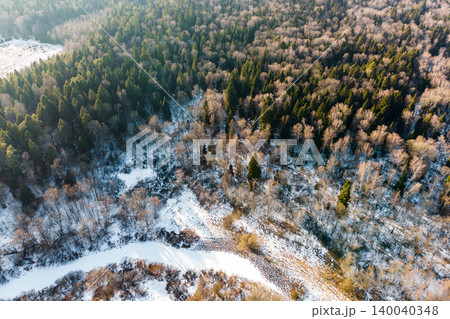 Aerial view of a serene winter forest landscape, showcasing a frozen oxbow lake winding through snow-dusted evergreen and deciduous trees under soft daylight Aerial view of a serene winter forest landscape, showcasing a frozen oxbow lake winding through snow-dusted evergreen and deciduous trees under soft daylight 140040348