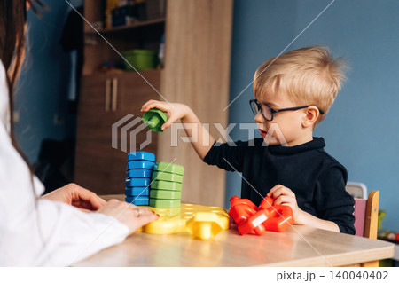 Preschool child stacking colorful building blocks with teacher's guidance in a bright classroom setting, engaging in developmental play activities Preschool child stacking colorful building blocks with teacher's guidance in a bright classroom setting, engaging in developmental play activities 140040402
