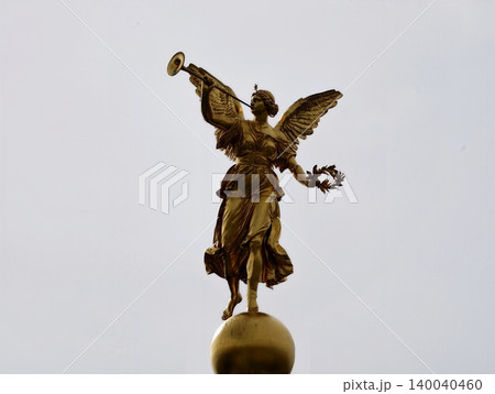 Decorative victory figure with trumpet and globe. Statue of angel celebrating triumph with symbolic motifs 140040460