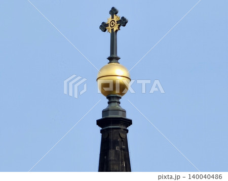 Gilded orb crowns slender tower. Architectural detail featuring luminous gold cross on tall spire Gilded orb crowns slender tower. Architectural detail featuring luminous gold cross on tall spire 140040486