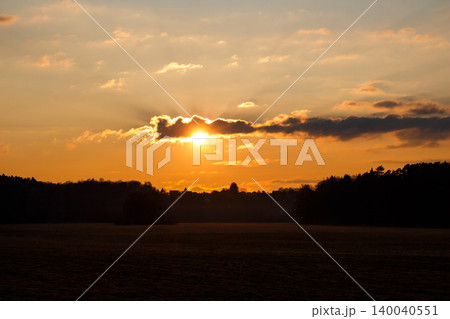 Dramatic sunset with golden rays piercing through dark clouds over a shadowy rural landscape. Breathtaking fiery sky at dusk, captivating nature Dramatic sunset with golden rays piercing through dark clouds over a shadowy rural landscape. Breathtaking fiery sky at dusk, captivating nature 140040551