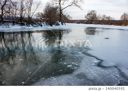 Frozen river surface displays intricate ice textures and reflections of leafless trees, capturing a cold winter day Frozen river surface displays intricate ice textures and reflections of leafless trees, capturing a cold winter day 140040591