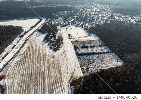 Winter aerial view of vast snow-dusted fields alongside a winding frozen waterway, with a distant village nestled among dark wintry woods Winter aerial view of vast snow-dusted fields alongside a winding frozen waterway, with a distant village nestled among dark wintry woods 140040620